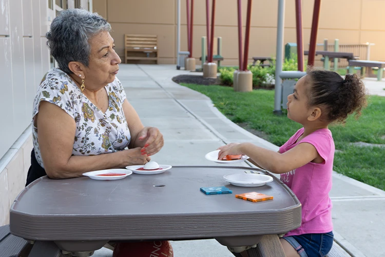 A mature woman and child sitting at a table, having a conversation and enjoying a meal together.